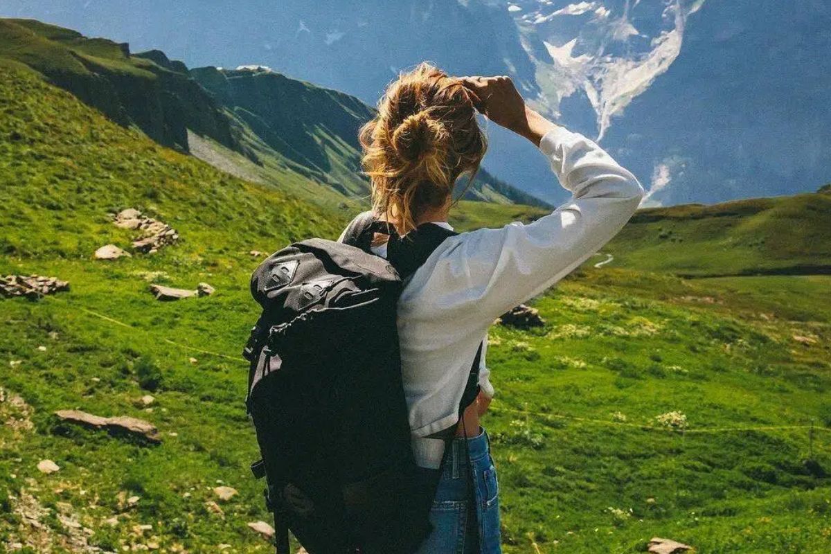 Umugore ugendana numufuka mwiza wo gutembera wagenewe abagore, bagenda kumurongo wumusozi hamwe nimisozi yicyatsi kibisi.